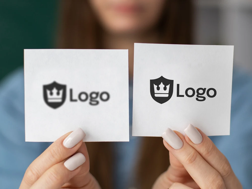 Two pieces of paper, one displaying a pixelated logo and the other a pixel perfect logo, are held by hands.