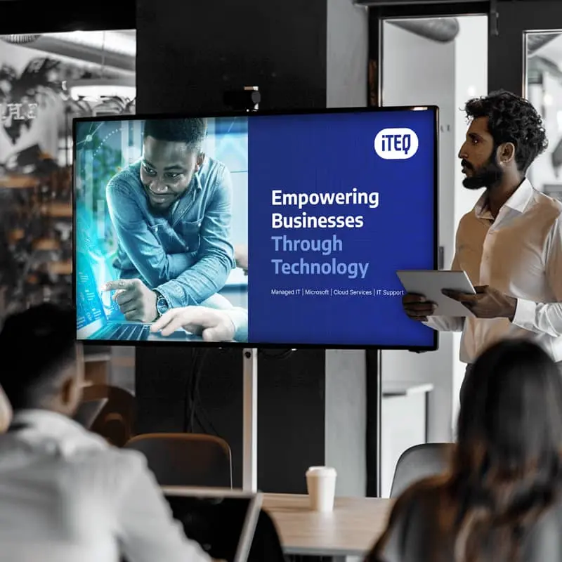 Business presentation on empowering businesses through technology, featuring a large screen displaying the presentation title and speakers interacting with digital content.