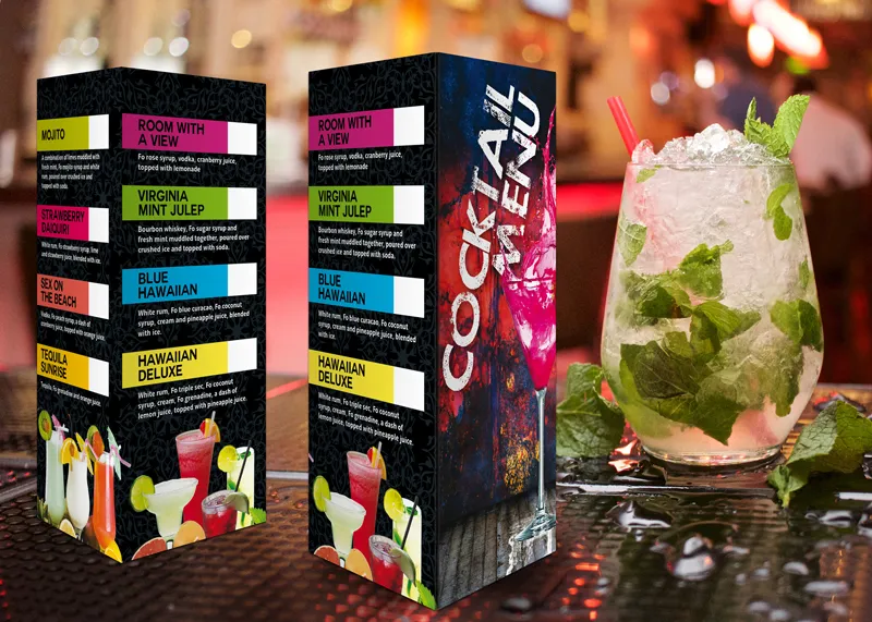 A vibrant cocktail menu and a mojito on a table. The menu lists colorful drink names and ingredients. The mojito is garnished with mint, set against a lively bar background.